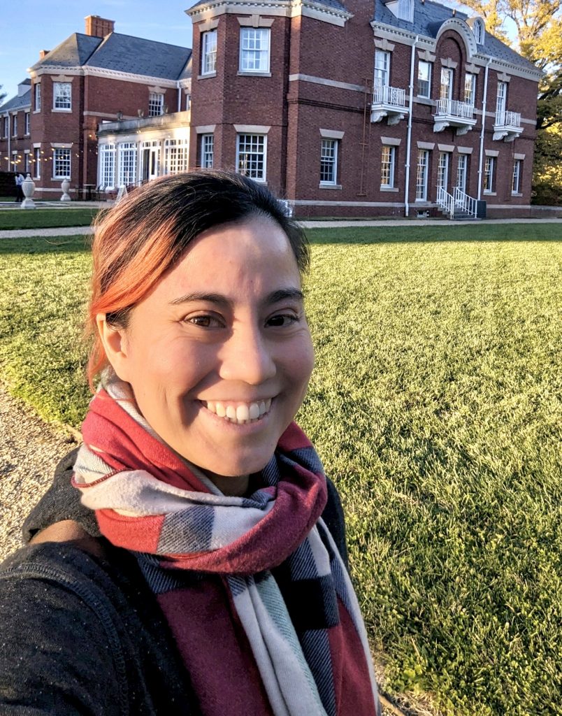 Smiling woman in scarf standing on lawn outside Allerton buildings at PLoP 2023
Conference